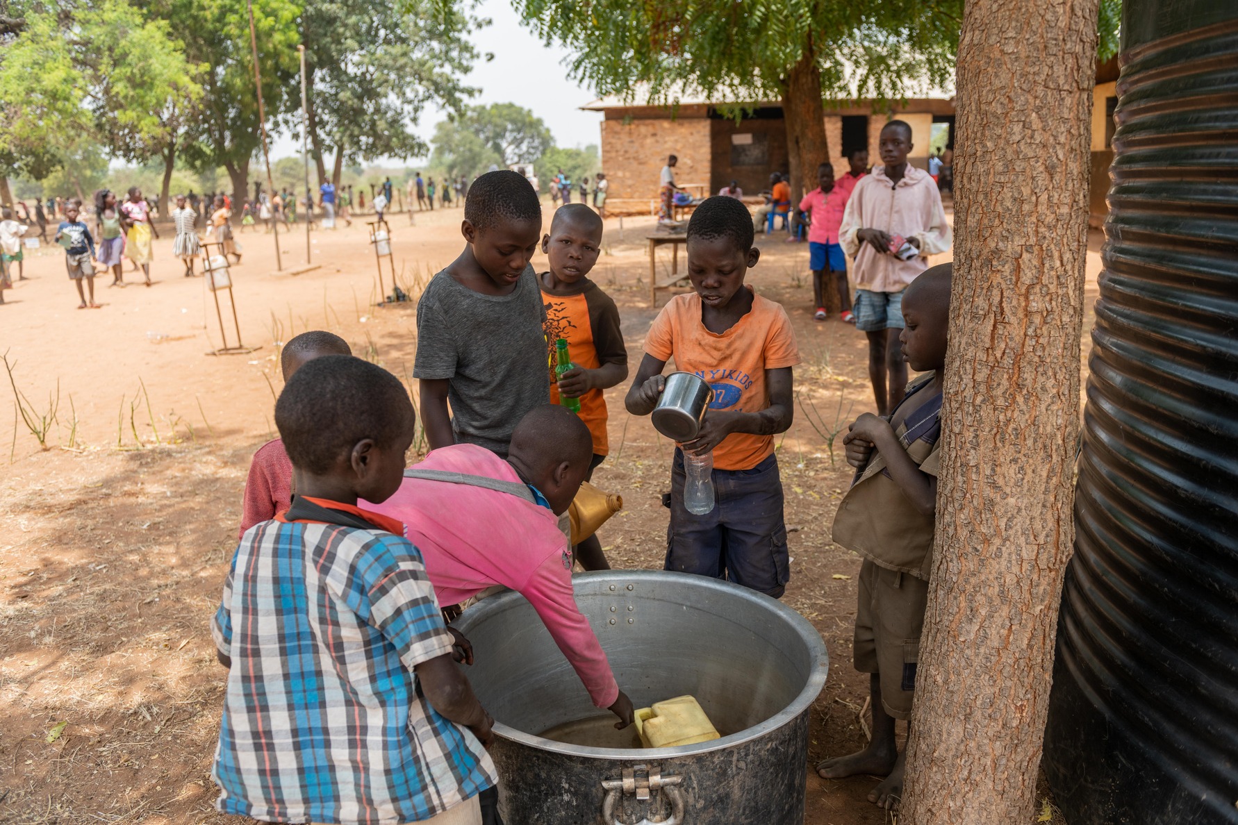Children draw water from a big saucepan.
