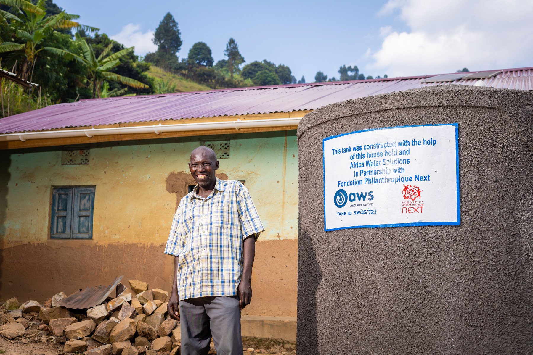 Ponsiano stands next to a rain water harvesting tank
